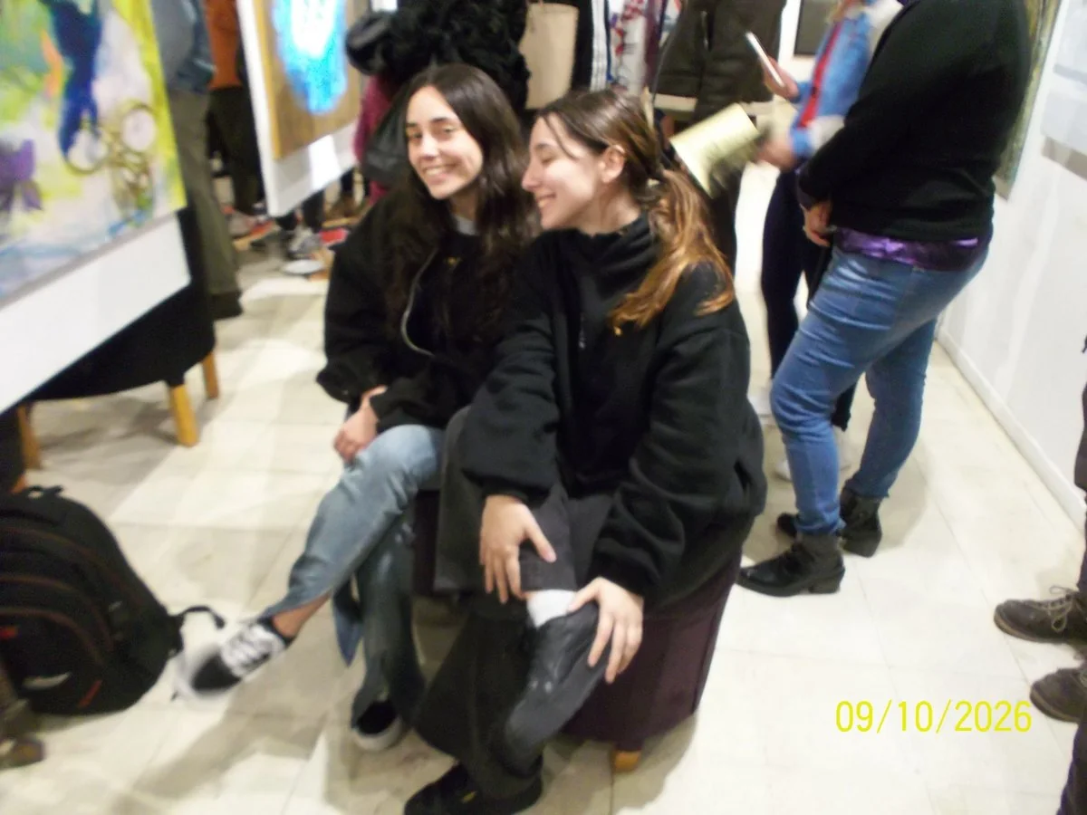 Delfina y Sofía sentadas juntas, sonriendo, en una muestra de arte